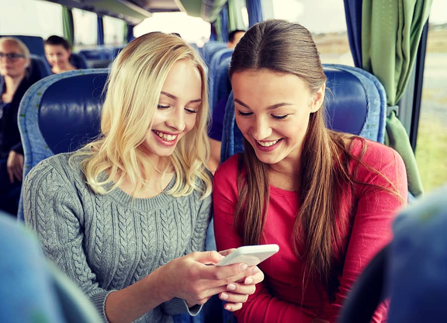 two passengers scroll through a phone on a bus rental